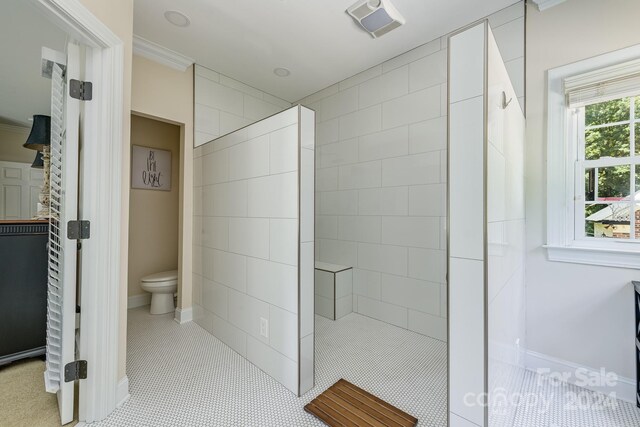 bathroom with tiled shower, toilet, and ornamental molding