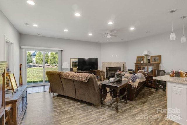 living room with dark wood-type flooring, ceiling fan, and a tiled fireplace