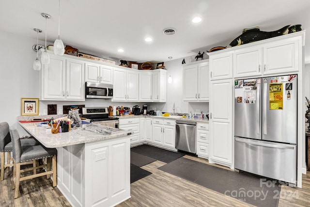 kitchen with white cabinetry, stainless steel appliances, a kitchen breakfast bar, dark hardwood / wood-style flooring, and kitchen peninsula