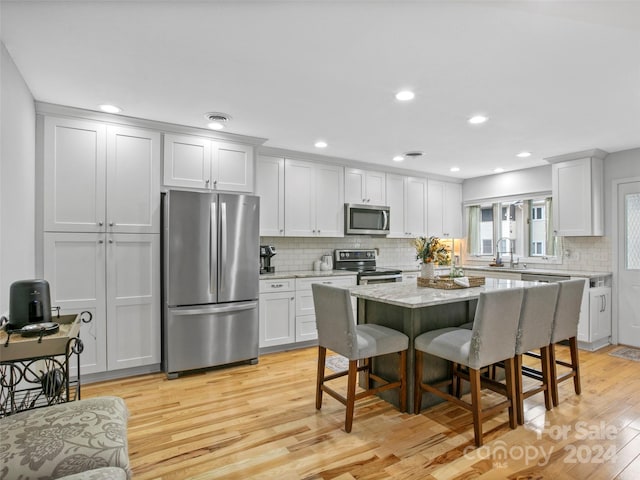 kitchen featuring light wood-type flooring, a center island, stainless steel appliances, and white cabinetry