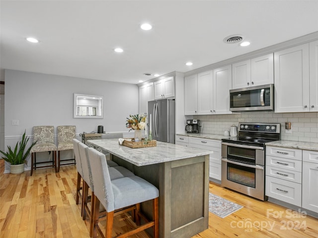 kitchen with light stone countertops, a kitchen island, stainless steel appliances, and light hardwood / wood-style flooring