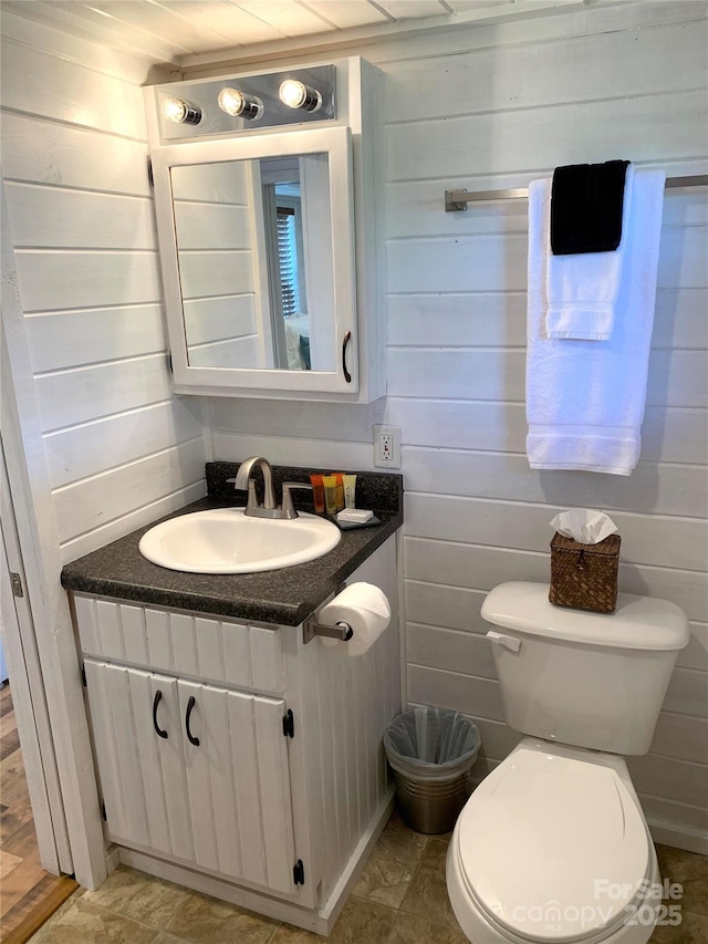 bathroom featuring vanity, toilet, and wood walls