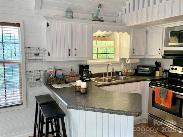 kitchen featuring white cabinetry, sink, stainless steel range with electric cooktop, kitchen peninsula, and plenty of natural light