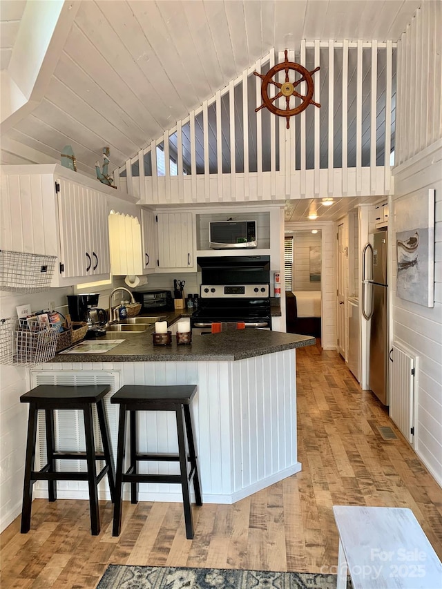 kitchen with white cabinetry, appliances with stainless steel finishes, a kitchen breakfast bar, and kitchen peninsula