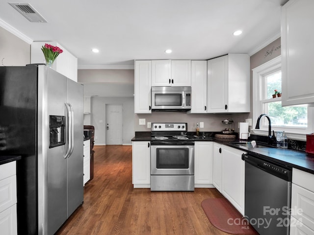 kitchen with ornamental molding, sink, dark wood-type flooring, appliances with stainless steel finishes, and white cabinets