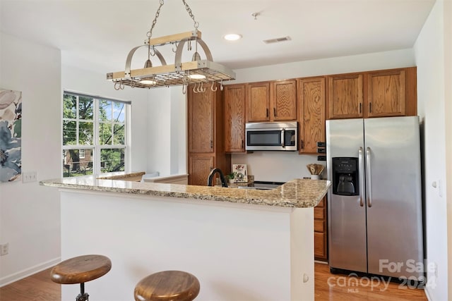 kitchen featuring a breakfast bar, stainless steel appliances, kitchen peninsula, light stone counters, and light wood-type flooring