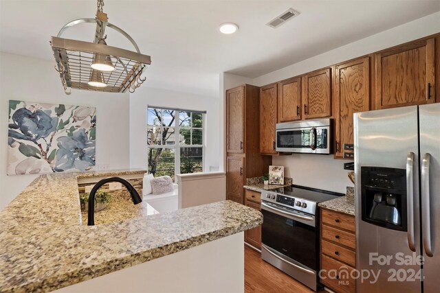 kitchen featuring light wood-type flooring, kitchen peninsula, stainless steel appliances, and light stone countertops