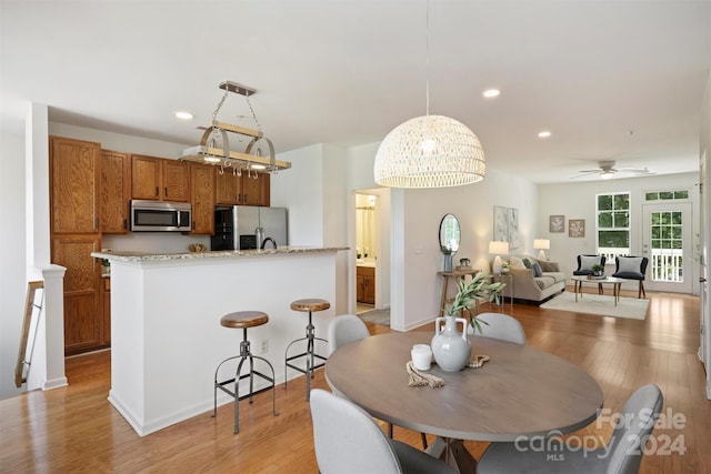 dining area with ceiling fan with notable chandelier and light hardwood / wood-style flooring