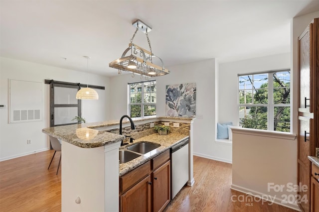 kitchen with light stone counters, light hardwood / wood-style floors, sink, pendant lighting, and stainless steel dishwasher