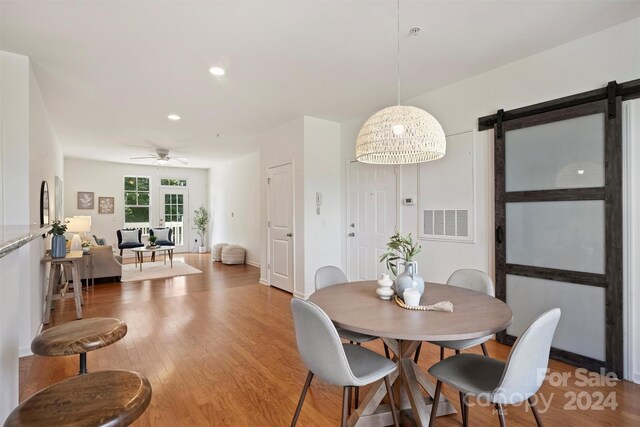 dining room featuring a barn door, ceiling fan, and hardwood / wood-style flooring