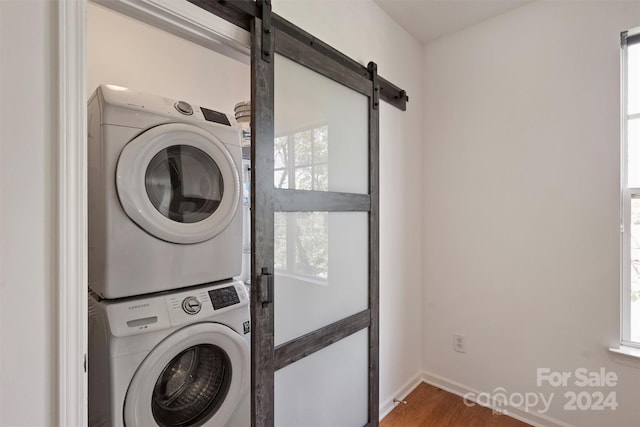 laundry area with a barn door, plenty of natural light, stacked washing maching and dryer, and wood-type flooring