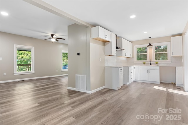 kitchen featuring decorative light fixtures, decorative backsplash, white cabinetry, and light hardwood / wood-style flooring