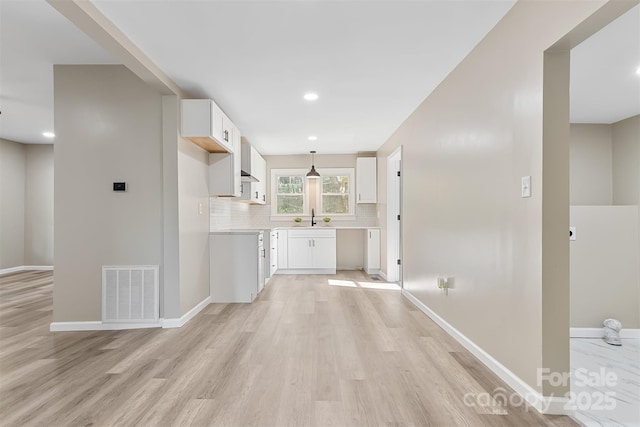 kitchen featuring white cabinets, light wood-type flooring, tasteful backsplash, and sink