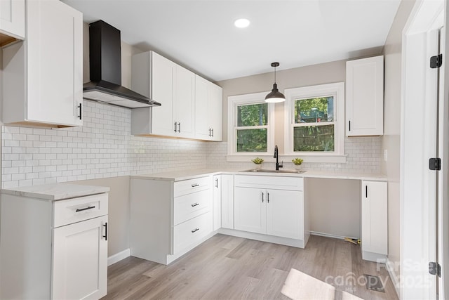 kitchen with wall chimney range hood, sink, light wood-type flooring, tasteful backsplash, and white cabinetry