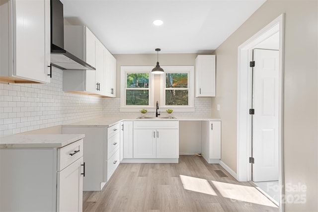 kitchen with white cabinetry, sink, pendant lighting, and wall chimney range hood