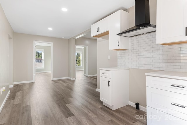 kitchen featuring backsplash, light hardwood / wood-style flooring, white cabinets, and wall chimney range hood