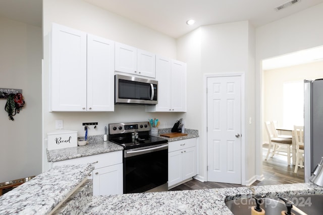 kitchen with white cabinetry, hardwood / wood-style flooring, light stone counters, and stainless steel appliances