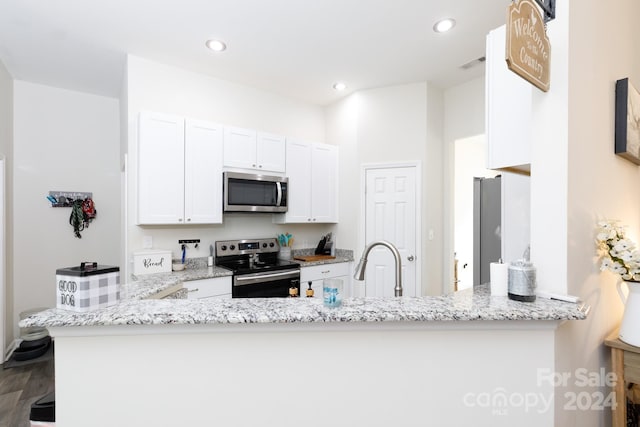 kitchen with light stone countertops, appliances with stainless steel finishes, kitchen peninsula, hardwood / wood-style flooring, and white cabinets