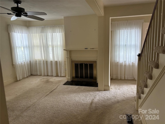 unfurnished living room with ceiling fan, light colored carpet, and a wealth of natural light