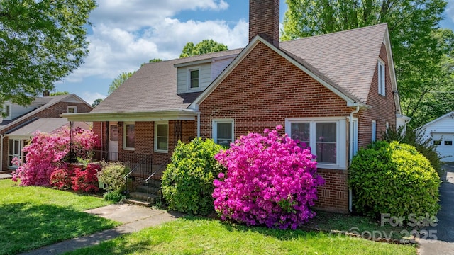 view of front of property with roof with shingles, a front lawn, a chimney, covered porch, and brick siding