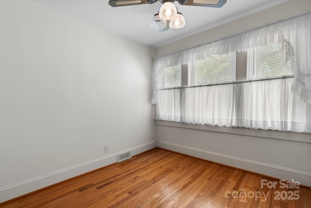 empty room featuring wood finished floors, visible vents, a ceiling fan, and baseboards