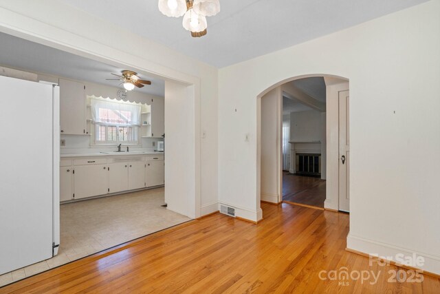 unfurnished dining area with visible vents, a sink, arched walkways, light wood-style floors, and ceiling fan