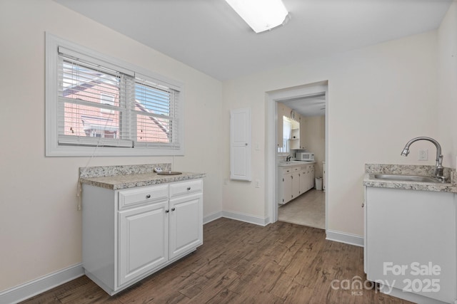 kitchen with white cabinetry, a sink, dark wood-style floors, and light countertops