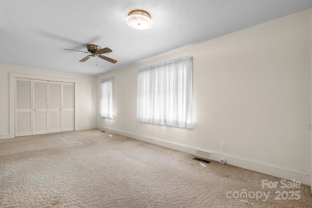 unfurnished bedroom featuring a closet, ceiling fan, carpet floors, baseboards, and visible vents