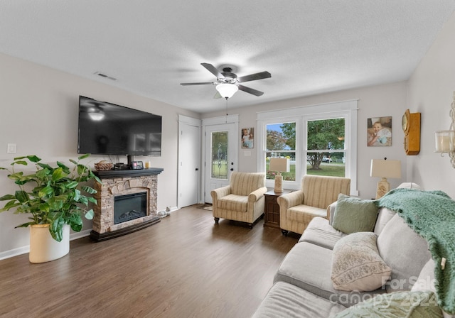 living room featuring a textured ceiling, ceiling fan, dark hardwood / wood-style floors, and a stone fireplace