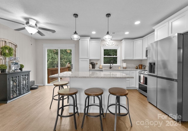 kitchen with a kitchen island, stainless steel appliances, ceiling fan, and white cabinets