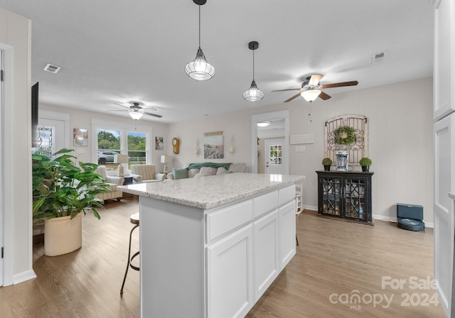 kitchen featuring a center island, light wood-type flooring, light stone counters, white cabinetry, and ceiling fan