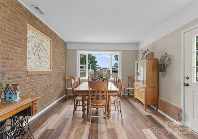 dining space featuring brick wall, crown molding, and hardwood / wood-style floors