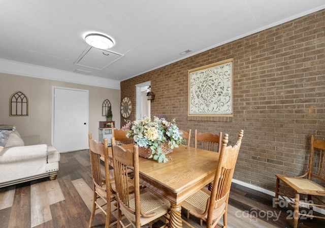 dining room with ornamental molding, hardwood / wood-style flooring, and brick wall