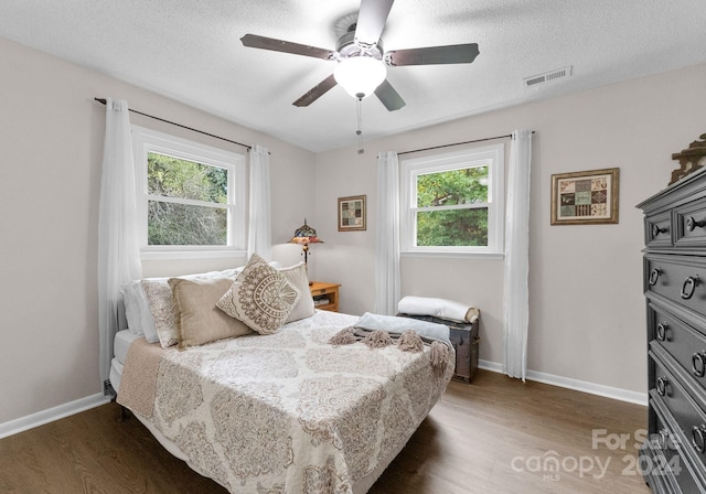 bedroom with dark wood-type flooring, multiple windows, ceiling fan, and a textured ceiling