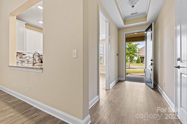 foyer with baseboards, visible vents, light wood-style flooring, crown molding, and a raised ceiling