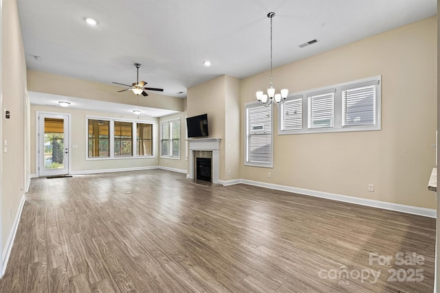 unfurnished living room featuring wood finished floors, visible vents, baseboards, a fireplace, and ceiling fan with notable chandelier