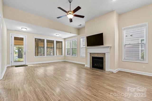 unfurnished living room featuring wood finished floors, baseboards, a high end fireplace, and a healthy amount of sunlight