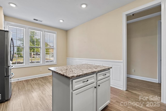 kitchen with light stone counters, a wainscoted wall, light wood finished floors, visible vents, and freestanding refrigerator