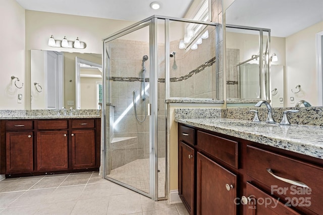 bathroom with tile patterned floors, a shower stall, two vanities, and a sink