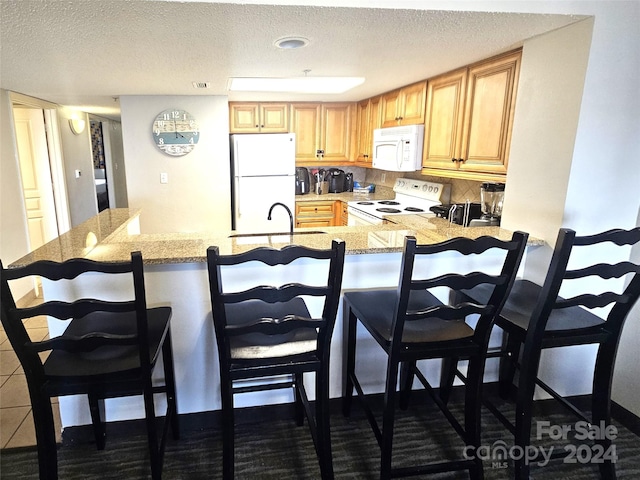 kitchen with white appliances, kitchen peninsula, sink, and a breakfast bar