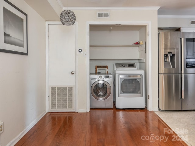 washroom featuring wood-type flooring, ornamental molding, and washing machine and clothes dryer