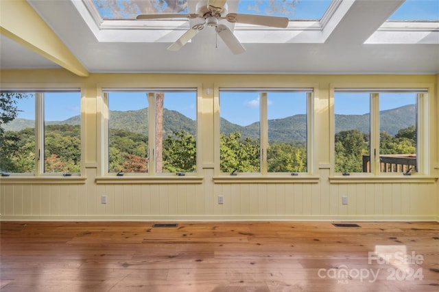 unfurnished sunroom featuring ceiling fan, a mountain view, lofted ceiling with skylight, and a healthy amount of sunlight