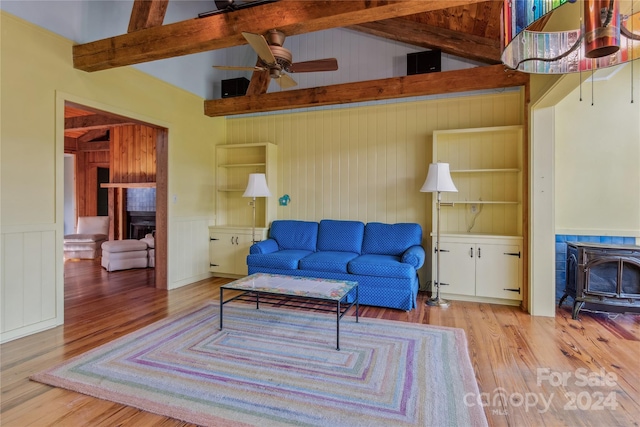 living room with a tiled fireplace, a wood stove, ceiling fan, lofted ceiling with beams, and hardwood / wood-style flooring