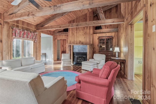 living room featuring a fireplace, wood-type flooring, wood walls, ceiling fan, and vaulted ceiling with beams