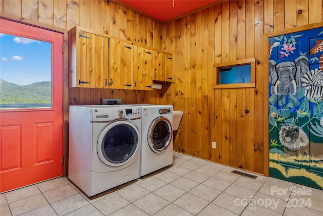 laundry area with washing machine and clothes dryer, cabinets, wooden walls, and light tile patterned flooring