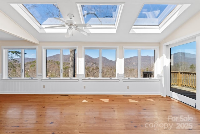 unfurnished sunroom with lofted ceiling with skylight, plenty of natural light, and a mountain view