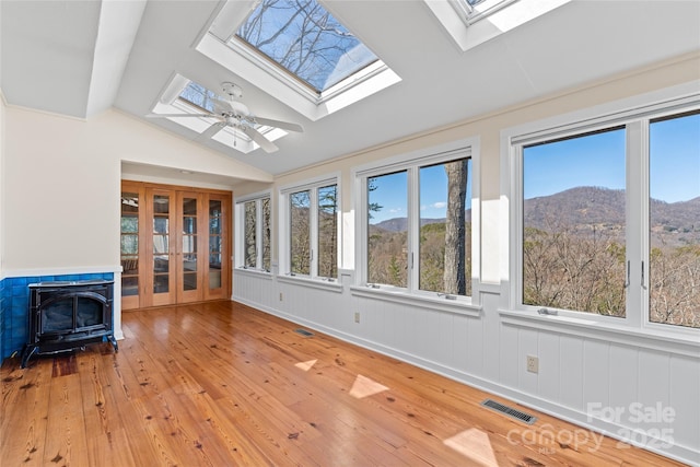 unfurnished sunroom with french doors, visible vents, a wood stove, a mountain view, and vaulted ceiling with skylight