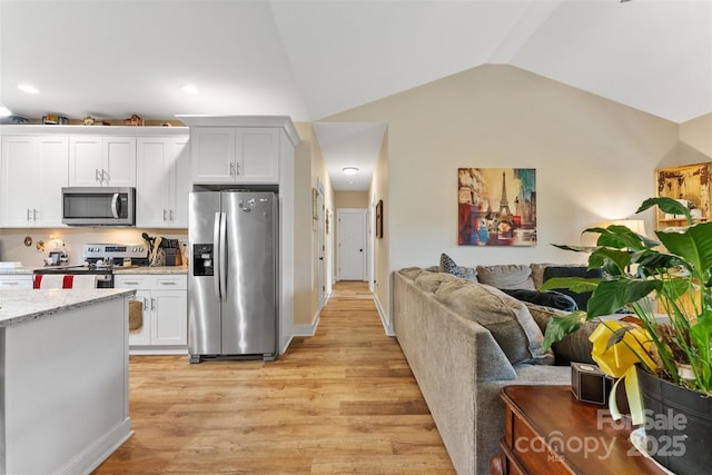 kitchen featuring light stone countertops, appliances with stainless steel finishes, vaulted ceiling, white cabinets, and light wood-type flooring