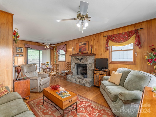 living room with light hardwood / wood-style floors, a fireplace, wood walls, and ceiling fan