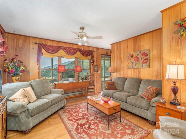 living room featuring ceiling fan, baseboard heating, wood walls, and light hardwood / wood-style floors